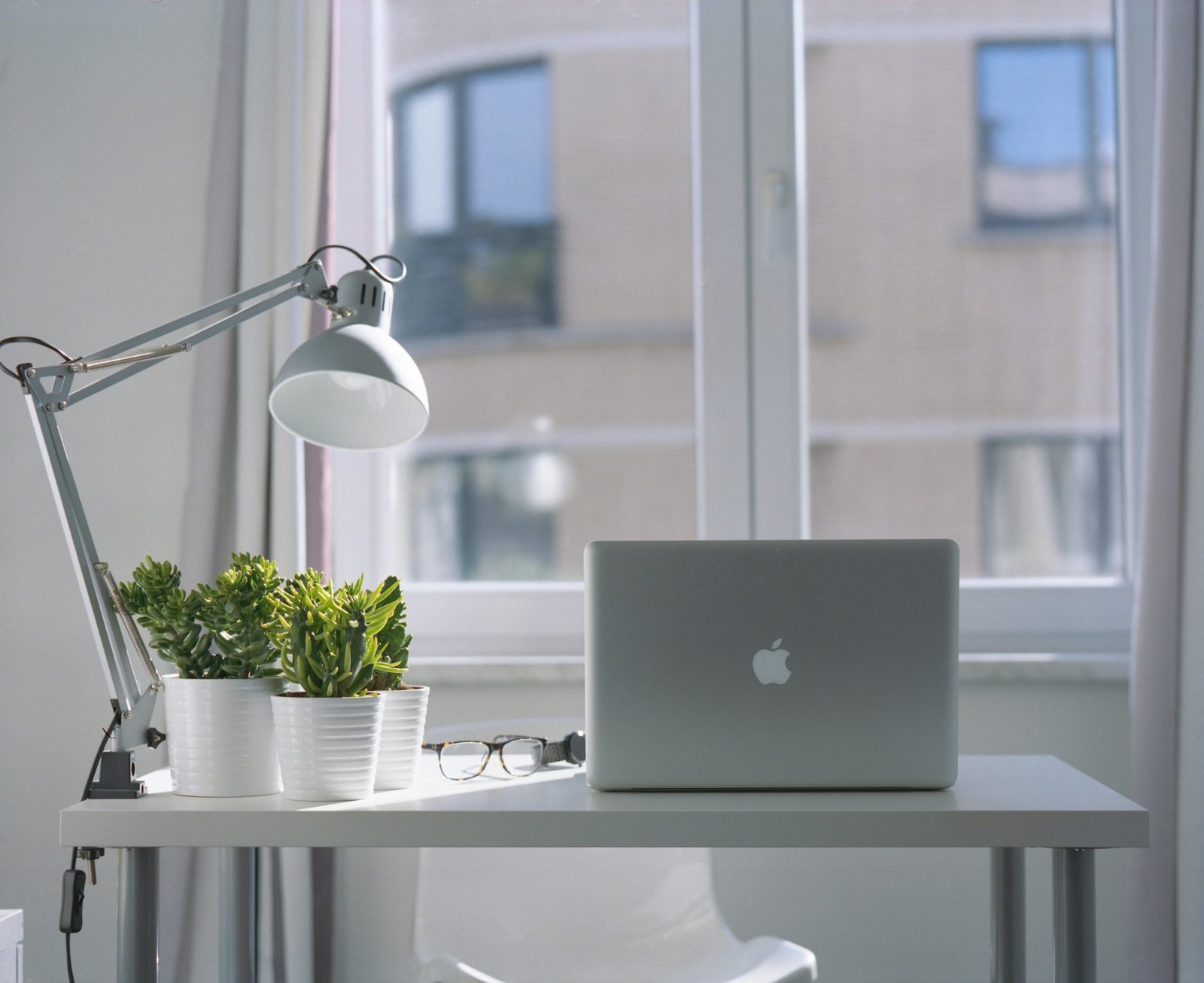 services-06 Bright modern workspace with laptop, potted plants, and desk lamp near a window.